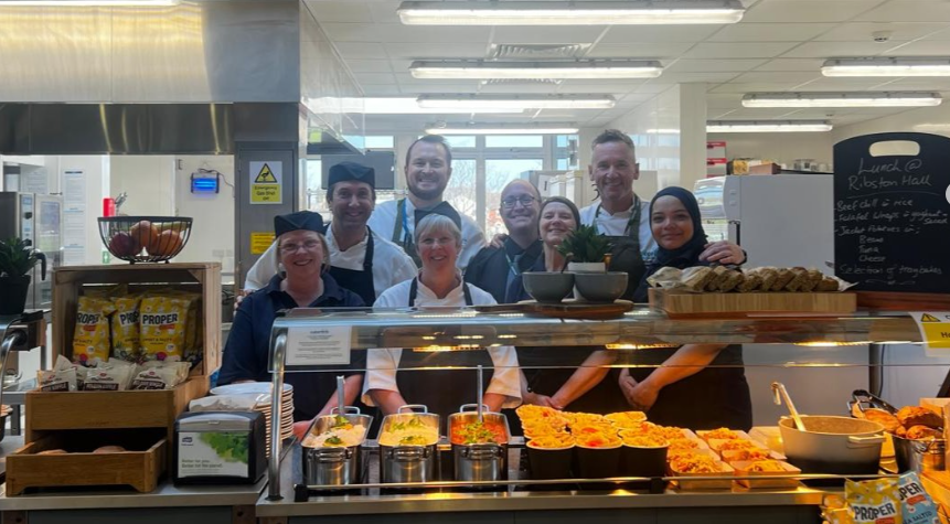 Our Caterlink standing behind our canteen counter, smiling towards the camera.