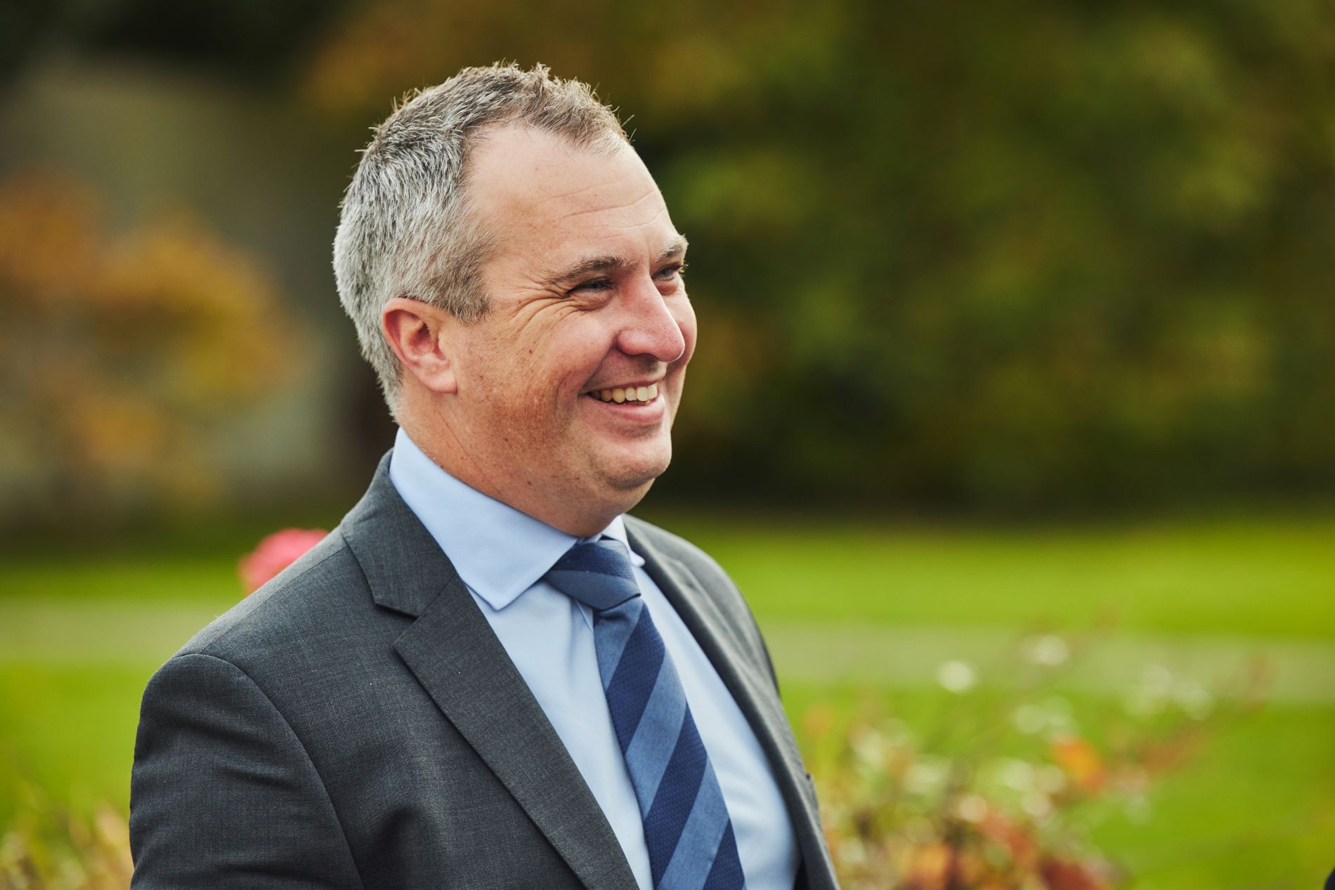 Picture of a smiling man looking away from the camera standing outside. 
